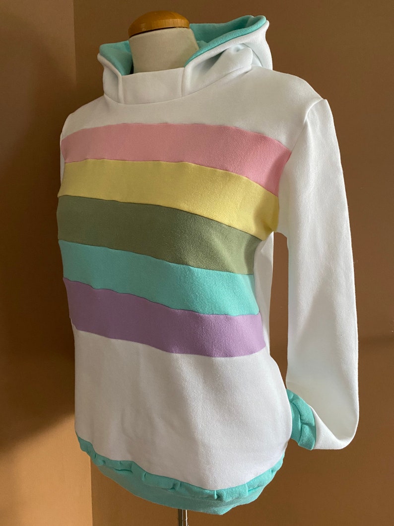 May include: White hoodie with a rainbow stripe pattern in pink, yellow, green, blue, and purple. The hoodie has a light blue hood lining.