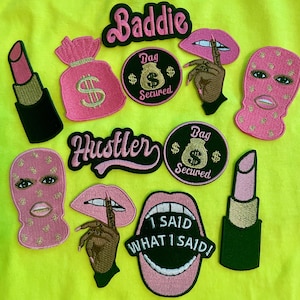 May include: A collection of embroidered patches on a neon yellow background, including pink lipstick tubes, money bags, ski masks, lips with fingers, and circular patches with the text Bag Secured, Baddie, Hustler, and I Said What I Said.