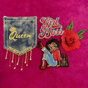 May include: A collection of four embroidered patches including a denim pocket shape with the word Queen and gold fringe, a Girl Boss script patch, a cartoon character in red clothing with a handbag, and a red rose with green leaves.