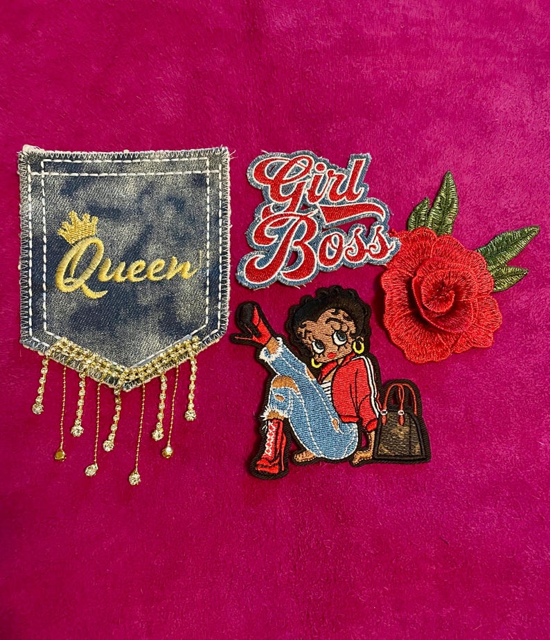 May include: A collection of four embroidered patches including a denim pocket shape with the word Queen and gold fringe, a Girl Boss script patch, a cartoon character in red clothing with a handbag, and a red rose with green leaves.