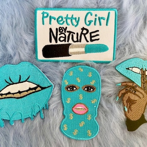 May include: Set of five embroidered iron-on patches. The patches feature a turquoise blue color scheme. One patch says "Pretty Girl by Nature" with a turquoise blue lipstick. Another patch is a turquoise blue mouth with gold teeth. Another patch is a turquoise blue face mask with gold dollar signs. Another patch is a turquoise blue mouth with a finger over it. The last patch is a brown hand with turquoise blue fingernails.