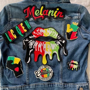 May include: A blue denim jacket adorned with colorful patches. Patches include the word "Melanin" in red script, a dripping lips design, and the words "Do it for the Culture" and "Juneteenth". Other patches feature a raised fist and the word "Love".