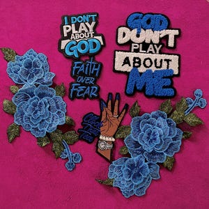 May include: A collection of embroidered patches including two large blue floral sprays with green leaves, a hand graphic with blue nails and a watch, and text patches reading I DON'T PLAY ABOUT GOD, FAITH OVER FEAR, GOD DON'T PLAY ABOUT ME, and Clock That Tea.