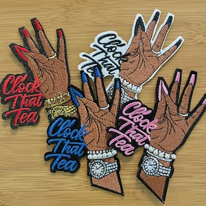 May include: Embroidered patches featuring a brown hand with long, painted nails. Each patch has a different nail color: red, blue, black, and pink. The text "Clock That Tea" is embroidered in various colors. The patches have a black border.