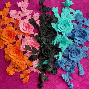 May include: A collection of four floral lace appliques in orange, pink, black, and blue-green. Each piece features intricate embroidered rose motifs with detailed petals and leafy stems, designed for sewing or decorative textile applications.