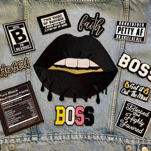 May include: A denim jacket adorned with various embroidered patches. Patches include the words "BOSS", "Chosen", "Faith", and "Blessed and Highly Favored". Other patches feature phrases and a black lip design.