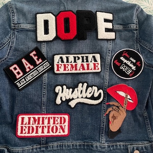 May include: A denim jacket adorned with various patches. Patches include the words "DOPE", "BAE", "ALPHA FEMALE", "Hustler", and "LIMITED EDITION". Other patches feature a red lip and a hand with a finger to the lips. The jacket is blue.