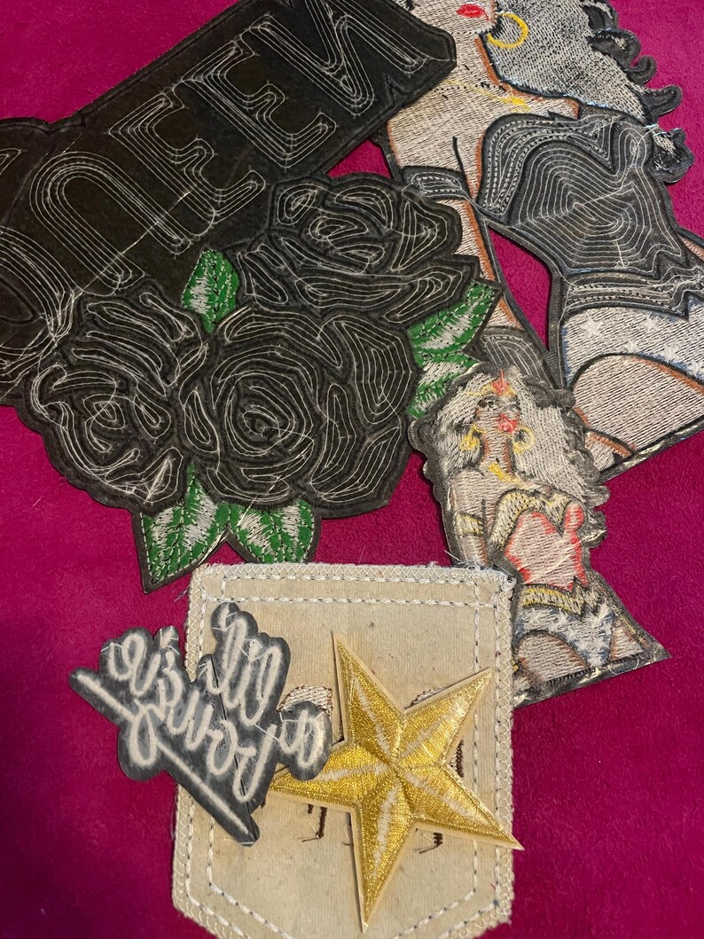 May include: A collection of embroidered patches including a black patch with the word QUEEN and black roses, two patches depicting a figure with long hair and gold jewelry, a small black patch with white script text, and a gold star on a beige fabric.