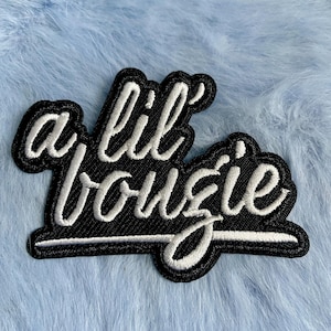 May include: A black and white embroidered patch with the text "a lil' bougie" in a cursive font.