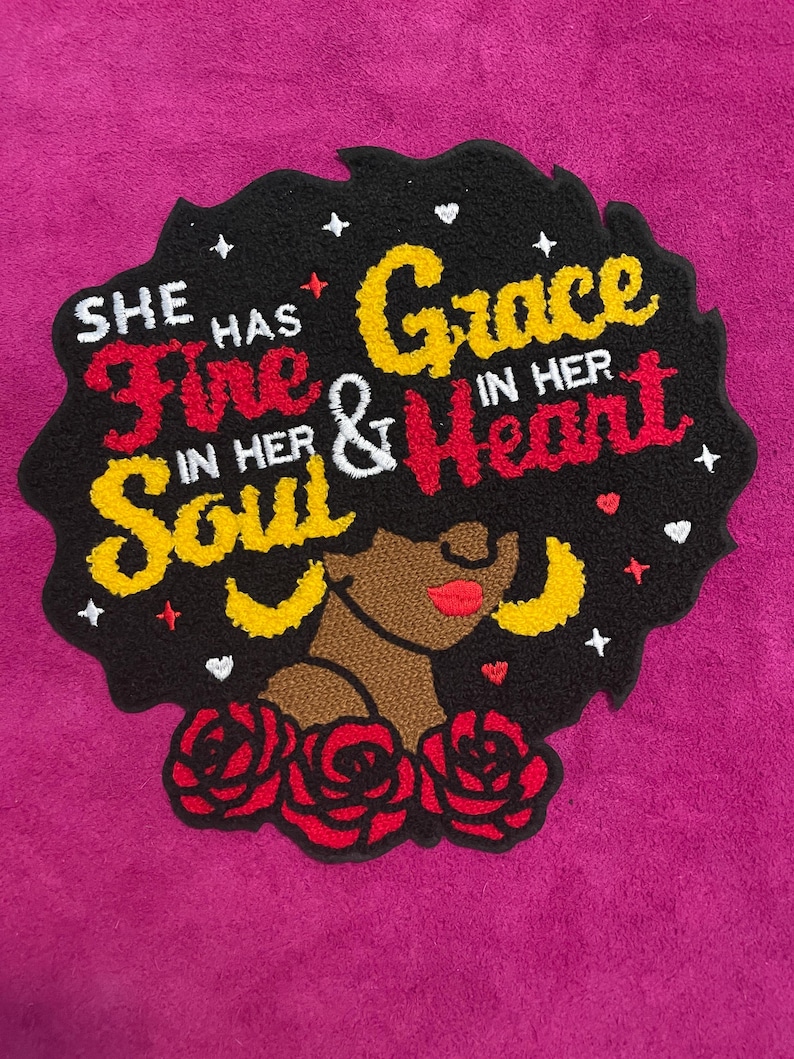 May include: A tufted rug featuring a profile of a person with dark skin, red lips, and yellow hoop earrings. The black hair background contains the text "SHE HAS FIRE IN HER SOUL & GRACE IN HER HEART" in red and yellow, accented by small white hearts and stars, with three red roses at the base.