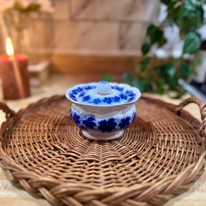 May include: A blue and white porcelain sugar bowl with a lid, sitting on a woven wicker tray.