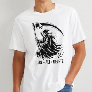 Puede incluir: Una camiseta blanca de manga corta con un gráfico negro de una parca encapuchada que sostiene una guadaña con la punta de un cursor de ordenador. El diseño incluye el texto CTRL + ALT + DELETE en una fuente pixelada debajo de la figura.
