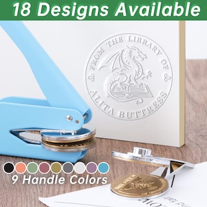 Peut inclure: Une presse à sceau bleu clair avec un sceau doré. La presse est à côté d'un livre blanc avec un sceau de dragon. Le texte "18 Designs Available" et "9 Handle Colors" sont visibles.