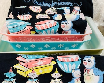 May include: Black graphic t-shirts and dish towels with a retro illustration of bowls, dishes, and bird characters. The text "Searching for Treasure" is featured on the shirts. The dish towels are folded and placed in colorful rectangular dishes.