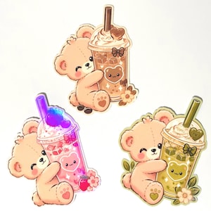 May include: Three die-cut stickers featuring light brown teddy bears hugging plastic cups of iced beverages. One cup is brown, one is pink with a strawberry, and one is green. Each bear has a smiling face, and each cup has a bear-shaped decal.