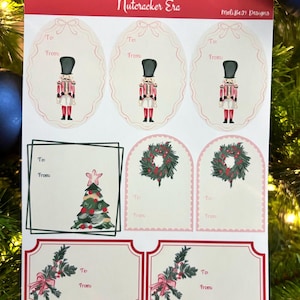 May include: A sheet of Christmas-themed gift tags and labels. Designs include nutcrackers, Christmas trees, wreaths, and sprigs with bows. The text "Nutcracker Era" and "Meli Ben Designs" are at the top. Each tag has space for "To" and "From".