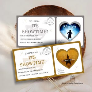 May include: Two rectangular gift tickets featuring theatre themes. The top ticket has grey accents, text reading TO LAURA ITS SHOWTIME, and a heart-shaped scratch-off area revealing Matilda. The bottom ticket has gold accents, text reading TO HANNAH ITS SHOWTIME, and a heart-shaped scratch-off area revealing Hamilton.