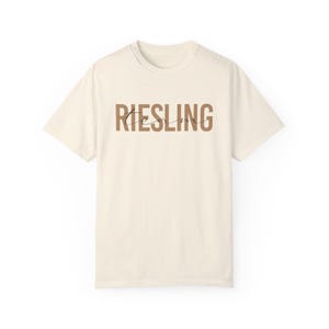 Op de afbeelding: Een crèmekleurig T-shirt met het woord "RIESLING" in bruin op de voorkant.
