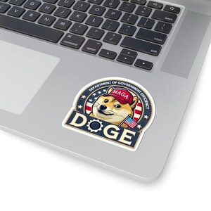 May include: A sticker featuring a Shiba Inu dog wearing a red "MAGA" hat and a small American flag. The dog is surrounded by a blue circle with white stars and the text "Department of Government Efficiency" and "DOGE".