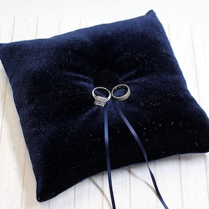 May include: A navy blue velvet ring pillow with two silver rings on top and two black satin ribbons.
