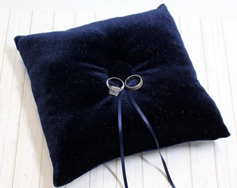 May include: A navy blue velvet ring pillow with two silver rings on top and two black satin ribbons.