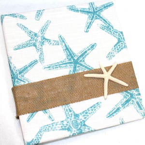 May include: A white canvas with a blue starfish pattern and a brown burlap ribbon. A white starfish is placed on top of the ribbon.
