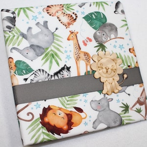May include: White wrapping paper with a jungle animal theme. The paper features a variety of animals including elephants, zebras, giraffes, lions, and monkeys. The paper also has green leaves and blue stars. A wooden lion cutout is attached to the paper.