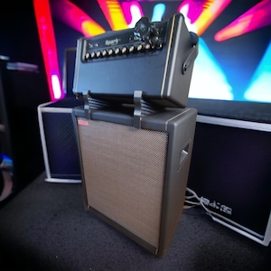 Può includere: Un amplificatore per chitarra nero con un cabinet per altoparlanti marrone. L'amplificatore ha una finitura dorata e il testo "Spark" sul davanti. Il cabinet per altoparlanti ha una griglia nera e un'etichetta rossa.