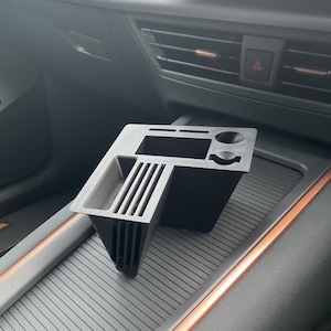 Könnte beinhalten: Schwarzer Auto-Organizer aus Kunststoff mit mehreren Fächern und einem kleinen Getränkehalter. Der Organizer befindet sich in der Mittelkonsole eines Autos.