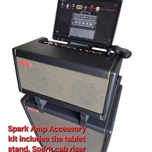 Könnte beinhalten: Ein schwarzer und goldener E-Gitarrenverstärker mit einem Tablet-Ständer oben drauf. Das Tablet zeigt einen Bildschirm mit einer Musik-App an. Der Text "Spark Amp Accessory kit includes the tablet stand, Spark cab riser and Spark Amp stand." ist unter dem Verstärker sichtbar.