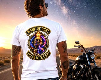 May include: White t-shirt with a graphic on the back featuring a skull, a cross, and the words "MADE OF DUST" and "FILLED WITH LIGHT" in a gold and blue design. A black motorcycle is parked on the side of the road.