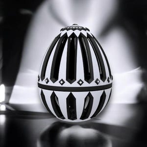 May include: A decorative egg-shaped object with a black and white striped pattern. The design features alternating vertical black stripes and white panels, with diamond-shaped accents. The top and bottom sections have a geometric design. The object is set against a blurred background.