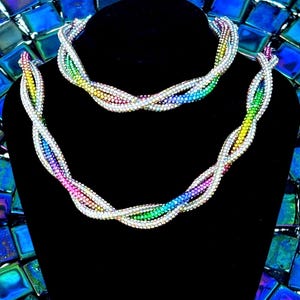 May include: A necklace and bracelet set featuring a twisted, multi-strand design. The jewelry is crafted from small, reflective beads in a vibrant rainbow gradient, transitioning through shades of red, orange, yellow, green, blue, and purple.
