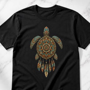 May include: A black short-sleeve t-shirt featuring a central graphic of a sea turtle. The turtle shell is decorated with a colorful, symmetrical mandala pattern in shades of orange, teal, and brown, with five dangling feathers below.