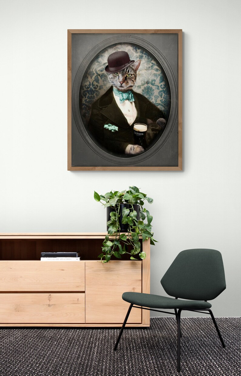 Puede incluir: Un retrato enmarcado de un gato con un sombrero de copa y un esmoquin, sosteniendo un vaso de Guinness. El gato est&aacute; sentado en un marco ovalado vintage con un fondo estampado.