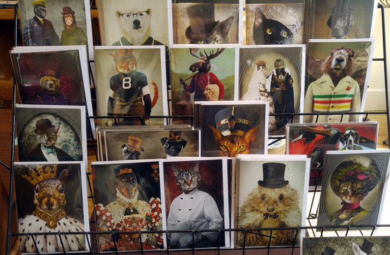 Puede incluir: Una colecci&oacute;n de impresiones de arte enmarcadas con varios animales vestidos con ropa. Las impresiones se muestran en un estante de metal negro. Algunos de los animales incluyen una ardilla, un gato, un perro, un alce y un tej&oacute;n.