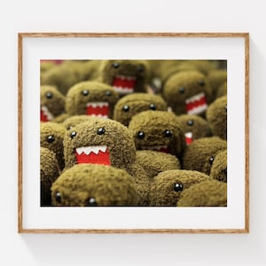 May include: A framed print featuring a close-up of multiple plush toys. The toys are brown with black eyes, white teeth, and red mouths. The toys have a fuzzy texture and are densely packed together.