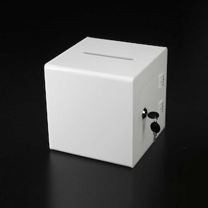 May include: A white, rectangular donation box with a slot on the top and a keyhole on the side. Two keys are inserted into the keyhole.