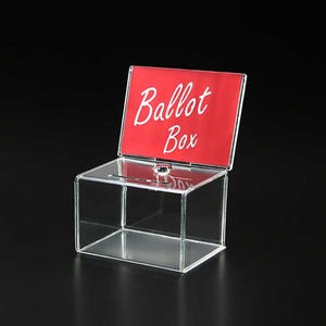 Op de afbeelding: Een transparante acryl stembus met een rood bord waarop "Ballot Box" in witte letters staat.