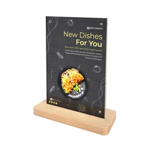 Puede incluir: Un letrero de mesa negro con una base de madera. El letrero anuncia "Nuevos platos para ti" con una imagen de un plato de arroz con salsa y champiñones. El texto dice "Plato de arroz con salsa y champiñones. Lorem ipsum dolor sit amet, consectetur adipiscing elit, sed do eiusmod tempor incididunt ut labore et dolomagna."