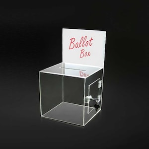 Puede incluir: Una urna transparente de acrílico con una ranura en la parte superior y una puerta con bisagras asegurada por una cerradura y llave. Las palabras "Ballot Box" están escritas en rojo en un letrero blanco.
