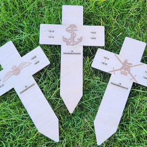 May include: Three wooden crosses with a white background and black text. The crosses are decorated with different military symbols and the text "1914 - 1918" and "1939 - 1945". The crosses also have the text "In Remembrance".