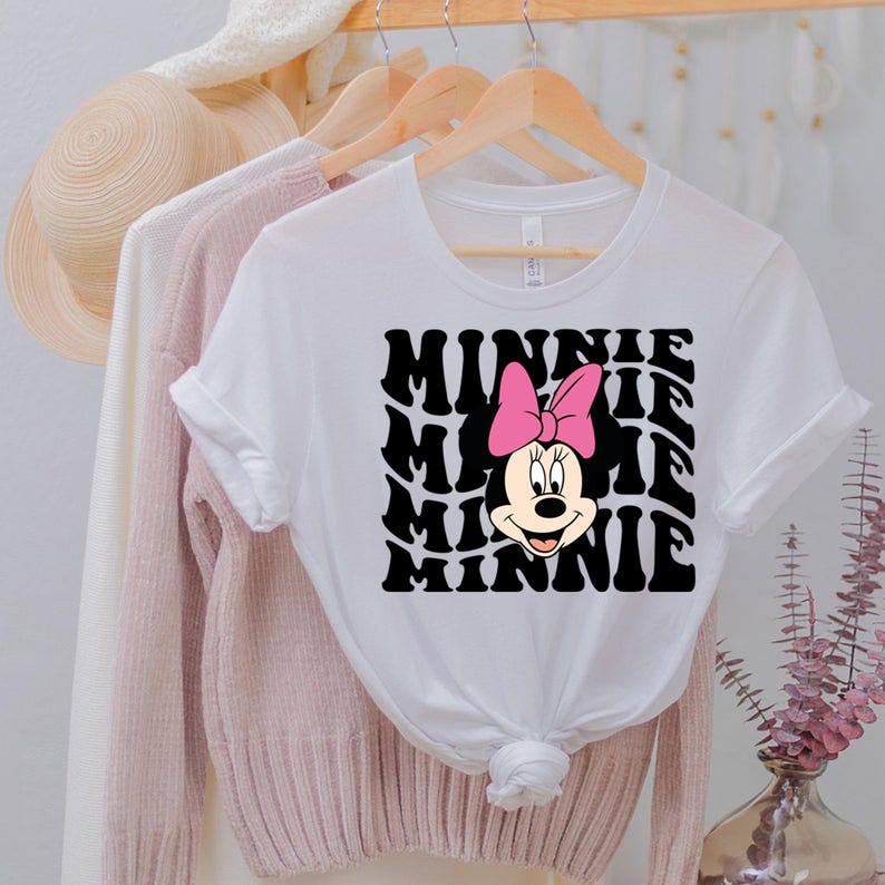 K&ouml;nnte beinhalten: Wei&szlig;es T-Shirt mit einer schwarz-wei&szlig;en Grafik von Minnie Mauss Gesicht und dem Wort "Minnie", das im Retro-Stil wiederholt wird.