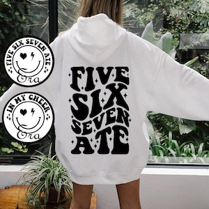 May include: White hoodie with a black graphic print on the back that says "Five Six Seven Ate" with a smiley face and lightning bolt design.