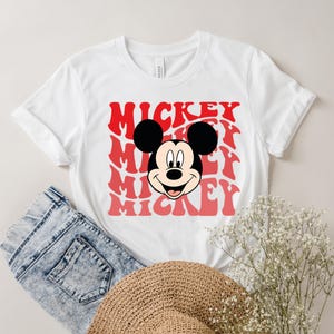 May include: White t-shirt with a red and white graphic of Mickey Mouse's face and the word "Mickey" repeated in a retro font.