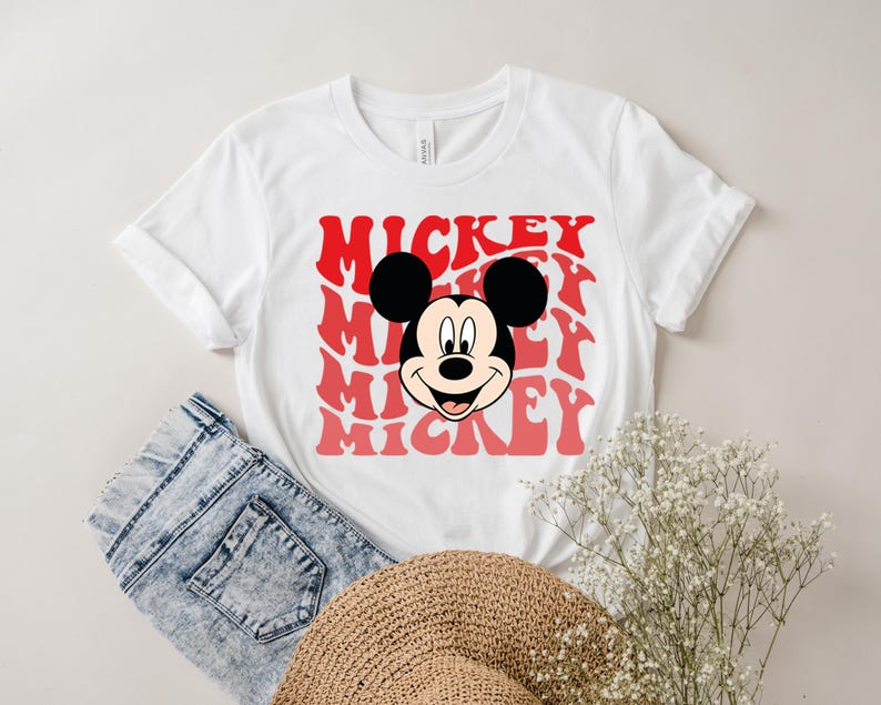May include: White t-shirt with a red and white graphic of Mickey Mouse's face and the word "Mickey" repeated in a retro font.