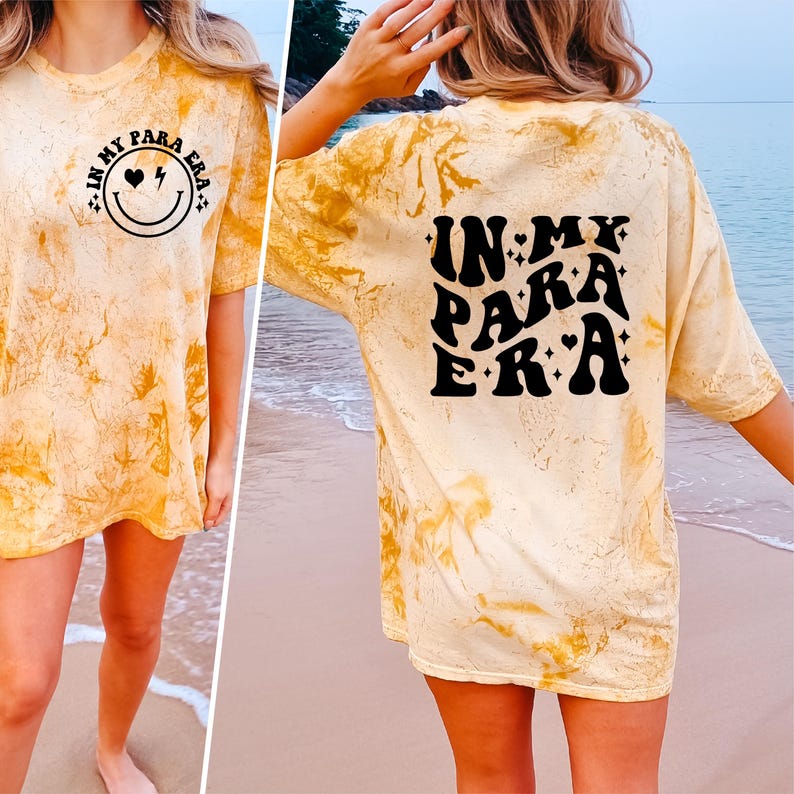 May include: A yellow tie-dye t-shirt with the text "In My Para Era" in black block letters with a heart and star design. The front of the shirt has a smiley face with a heart and lightning bolt.