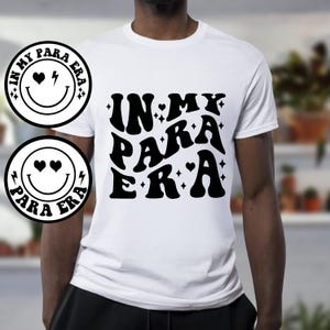 May include: White t-shirt with black text that reads "In My Para Era" in a retro font. The text is surrounded by small black hearts and stars.