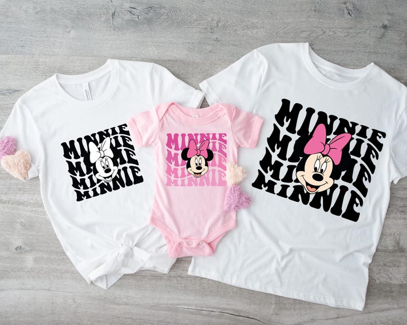 K&ouml;nnte beinhalten: Drei wei&szlig;e T-Shirts mit einer schwarz-wei&szlig;en Grafik von Minnie Maus mit dem Wort "Minnie", das in einem Retro-Stil wiederholt wird. Das kleinste Shirt ist rosa und hat kurze &Auml;rmel. Die beiden gr&ouml;&szlig;eren Shirts haben lange &Auml;rmel.