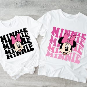 K&ouml;nnte beinhalten: Zwei wei&szlig;e T-Shirts mit einem schwarz-wei&szlig;en Minnie Mouse-Motiv auf dem einen und einem rosa-wei&szlig;en Minnie Mouse-Motiv auf dem anderen. Beide Shirts zeigen das Wort "Minnie" in einer Retro-Schrift wiederholt.
